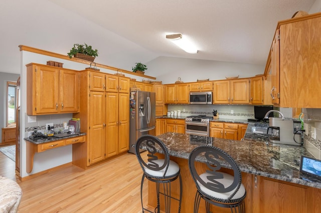 kitchen with a peninsula, light wood-style flooring, dark stone counters, vaulted ceiling, and appliances with stainless steel finishes