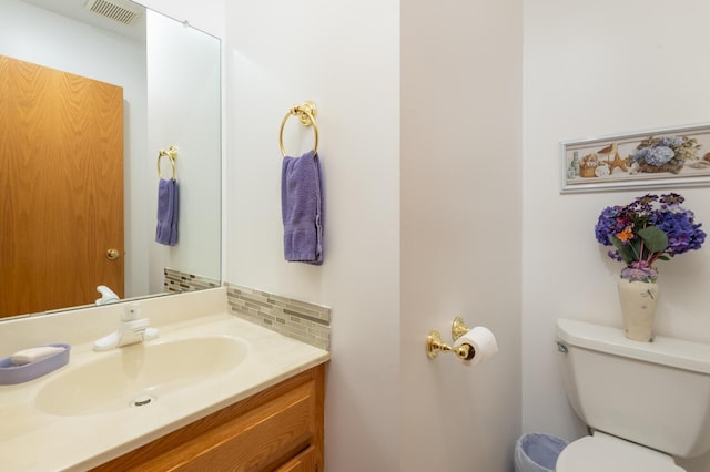 half bathroom with vanity, toilet, visible vents, and tasteful backsplash