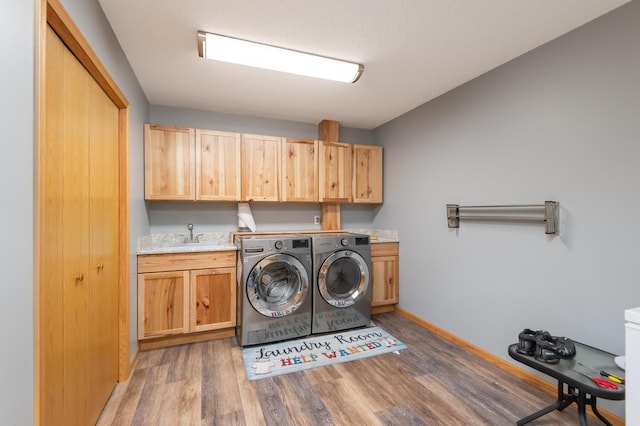 clothes washing area featuring wood finished floors, baseboards, cabinet space, a sink, and washer and dryer