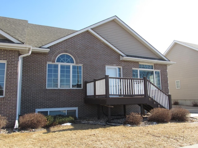 exterior space featuring brick siding, a deck, stairs, and roof with shingles