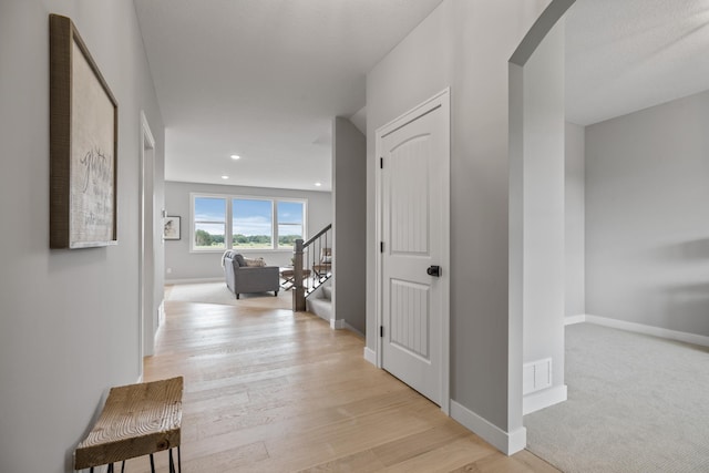 hall featuring visible vents, light wood-style flooring, arched walkways, baseboards, and stairs