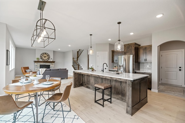 kitchen featuring light wood finished floors, dark brown cabinets, a stone fireplace, stainless steel refrigerator with ice dispenser, and arched walkways