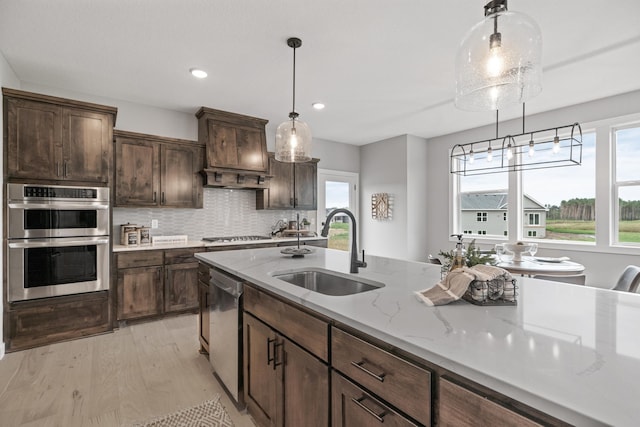 kitchen with light wood-type flooring, a sink, tasteful backsplash, stainless steel appliances, and hanging light fixtures