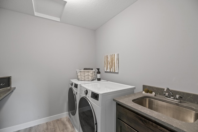 laundry room featuring baseboards, separate washer and dryer, a sink, light wood-style floors, and a textured ceiling