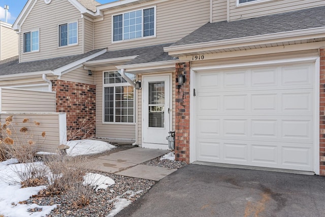 doorway to property featuring brick siding, driveway, and a shingled roof