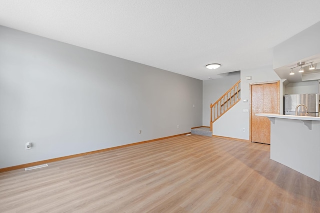 unfurnished living room with visible vents, baseboards, light wood-style floors, and stairs