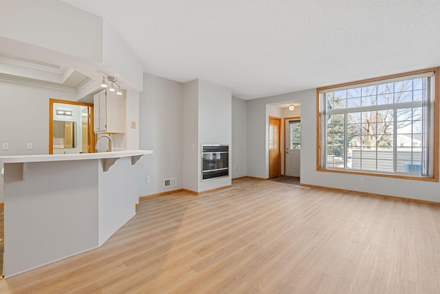 unfurnished living room with light wood finished floors, visible vents, baseboards, and a glass covered fireplace