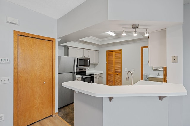 kitchen with light countertops, a kitchen bar, appliances with stainless steel finishes, a peninsula, and wood finished floors