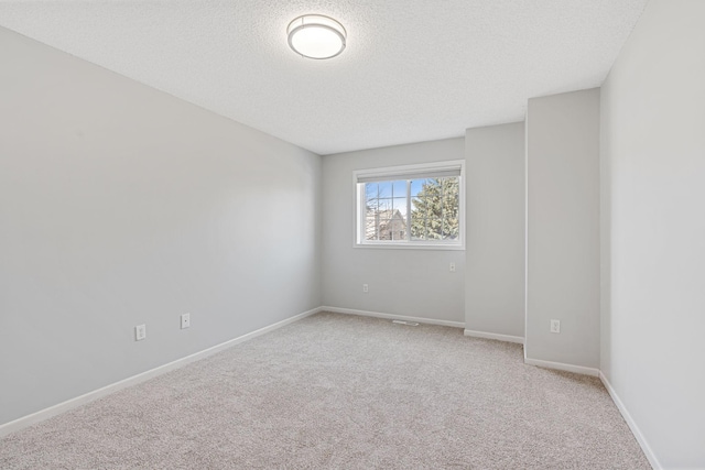 spare room featuring baseboards, light carpet, and a textured ceiling