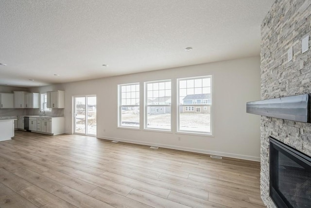 unfurnished living room featuring a stone fireplace, light wood-style flooring, baseboards, and a textured ceiling