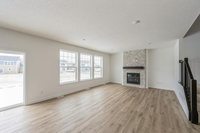 unfurnished living room with baseboards, a textured ceiling, a fireplace, and light wood finished floors