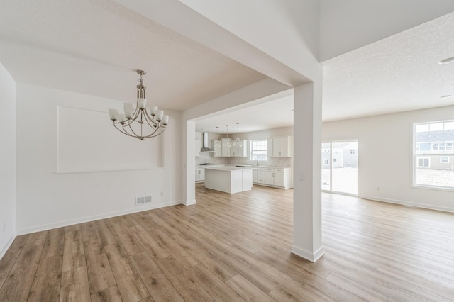 unfurnished living room with light wood finished floors, a chandelier, baseboards, and a sink