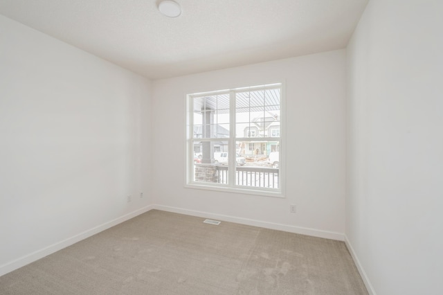 spare room with visible vents, baseboards, and light carpet