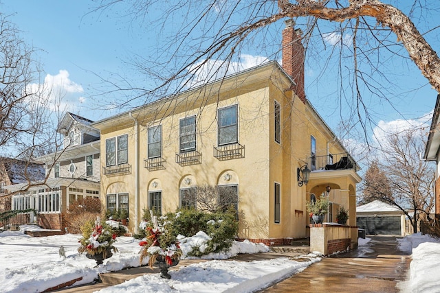 view of front of house featuring an outbuilding, stucco siding, a detached garage, and a chimney