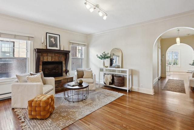 living room with ornamental molding, wood finished floors, arched walkways, a fireplace, and baseboards