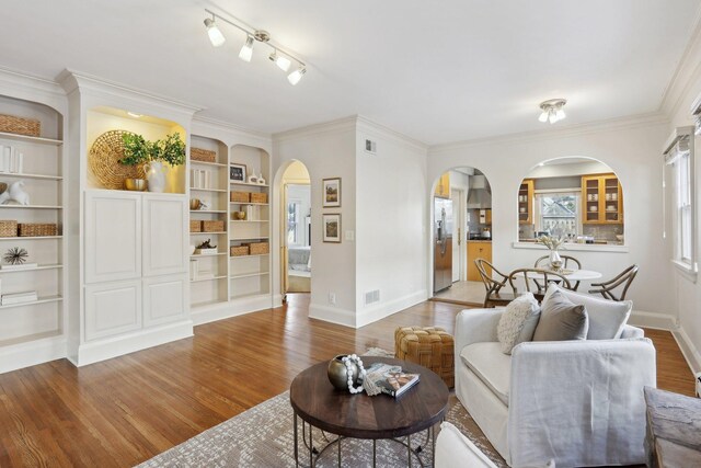 living area with visible vents, crown molding, baseboards, wood finished floors, and arched walkways