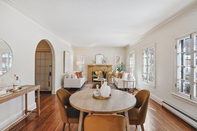 dining area featuring wood finished floors, baseboards, arched walkways, ornamental molding, and baseboard heating