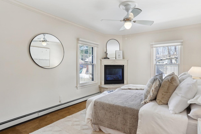 bedroom featuring a ceiling fan, baseboard heating, a glass covered fireplace, and crown molding