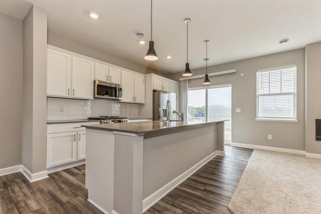 kitchen with decorative backsplash, appliances with stainless steel finishes, an island with sink, and white cabinetry