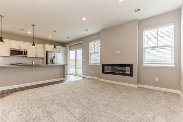 unfurnished living room with a glass covered fireplace, recessed lighting, carpet flooring, and baseboards