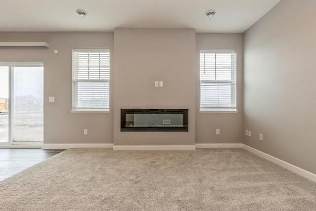 unfurnished living room featuring a glass covered fireplace, a healthy amount of sunlight, baseboards, and carpet