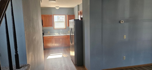 kitchen with brown cabinets, a sink, wood finished floors, freestanding refrigerator, and light countertops