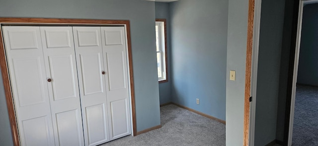 unfurnished bedroom with a closet, baseboards, and light colored carpet