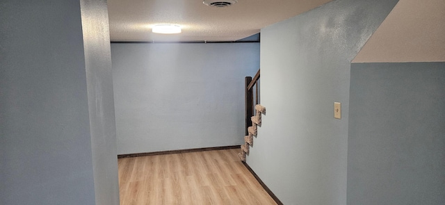 hall featuring baseboards, visible vents, light wood finished floors, and a textured ceiling