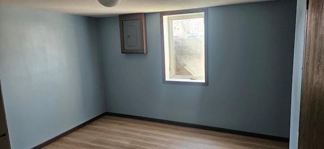 spare room featuring electric panel, baseboards, a textured ceiling, and light wood-style flooring