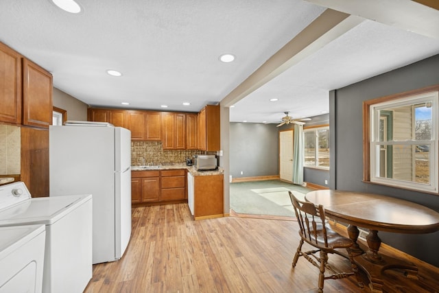 kitchen with brown cabinetry, light wood finished floors, freestanding refrigerator, washing machine and dryer, and tasteful backsplash