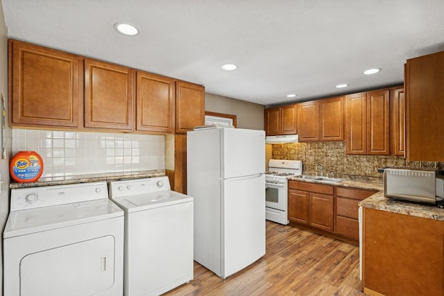 kitchen with light wood finished floors, extractor fan, washing machine and dryer, white appliances, and a sink