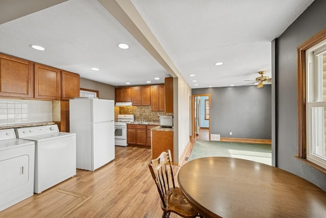 kitchen with light wood-type flooring, brown cabinets, washer and dryer, under cabinet range hood, and white appliances