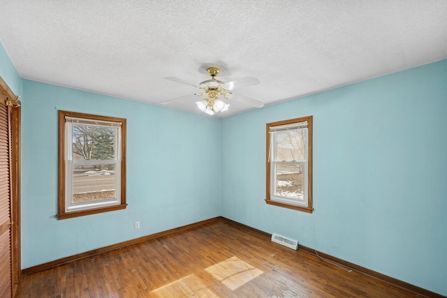 spare room with visible vents, baseboards, a textured ceiling, and wood finished floors