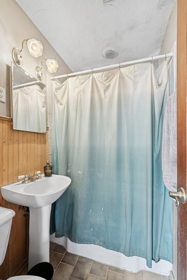 bathroom with a wainscoted wall, wood walls, toilet, a shower with curtain, and a textured ceiling