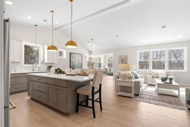 kitchen with gray cabinetry, open floor plan, a breakfast bar area, light wood finished floors, and light countertops