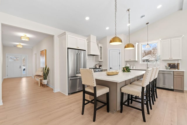 kitchen with custom range hood, a center island, stainless steel appliances, a breakfast bar area, and vaulted ceiling