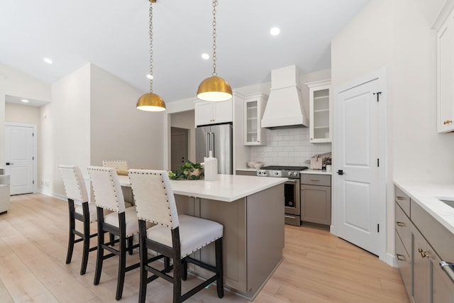 kitchen with high end appliances, custom exhaust hood, vaulted ceiling, a kitchen breakfast bar, and light wood-type flooring