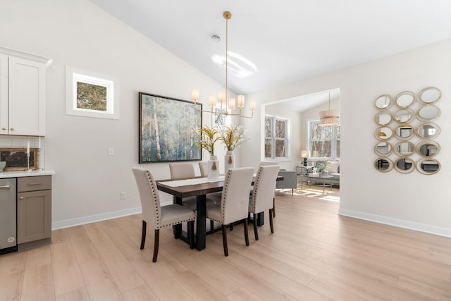 dining area featuring light wood finished floors, a chandelier, baseboards, and vaulted ceiling