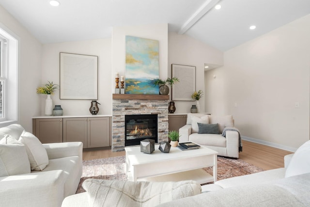 living room featuring baseboards, vaulted ceiling with beams, recessed lighting, a glass covered fireplace, and light wood-type flooring