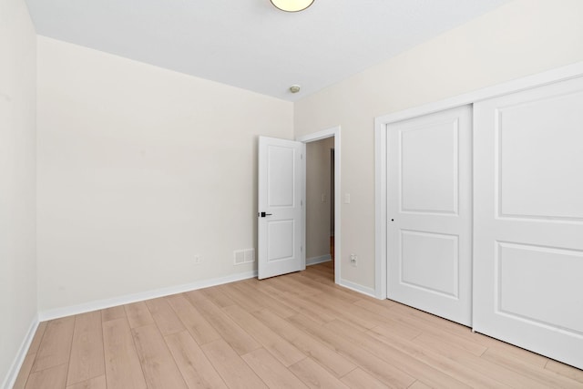 unfurnished bedroom with light wood finished floors, visible vents, a closet, and baseboards