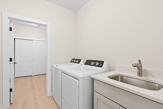 clothes washing area featuring washer and dryer, light wood finished floors, and a sink