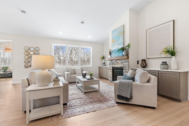 living room featuring a stone fireplace, vaulted ceiling, plenty of natural light, and light wood-type flooring