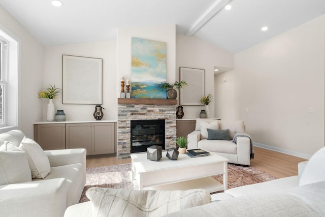 living area featuring baseboards, light wood finished floors, lofted ceiling with beams, recessed lighting, and a stone fireplace