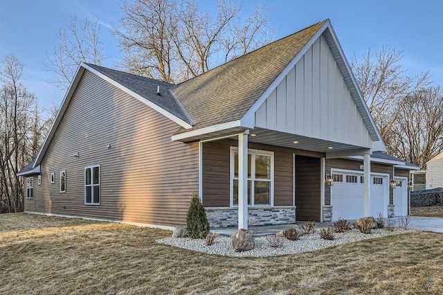 view of side of property with a shingled roof, covered porch, driveway, stone siding, and an attached garage