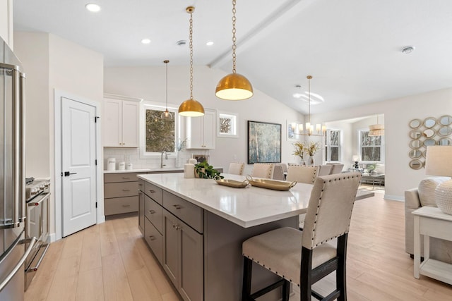 kitchen with lofted ceiling with beams, open floor plan, a kitchen breakfast bar, gray cabinetry, and light wood-style flooring