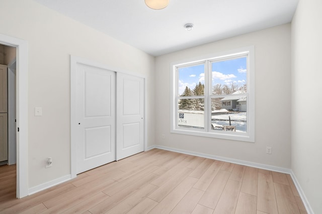 unfurnished bedroom with a closet, baseboards, and light wood finished floors