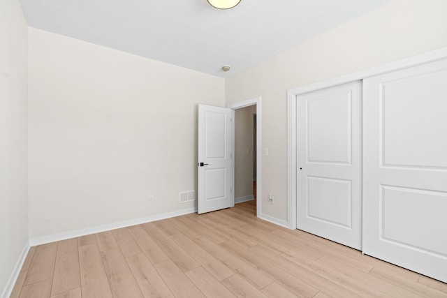 unfurnished bedroom featuring a closet, light wood-style flooring, baseboards, and visible vents