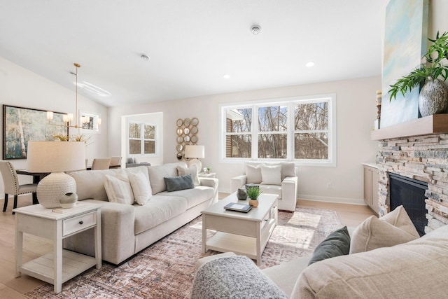living room featuring plenty of natural light, light wood-style flooring, a stone fireplace, and vaulted ceiling