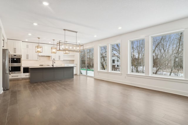 kitchen with a kitchen island with sink, stainless steel appliances, dark wood finished floors, and white cabinetry