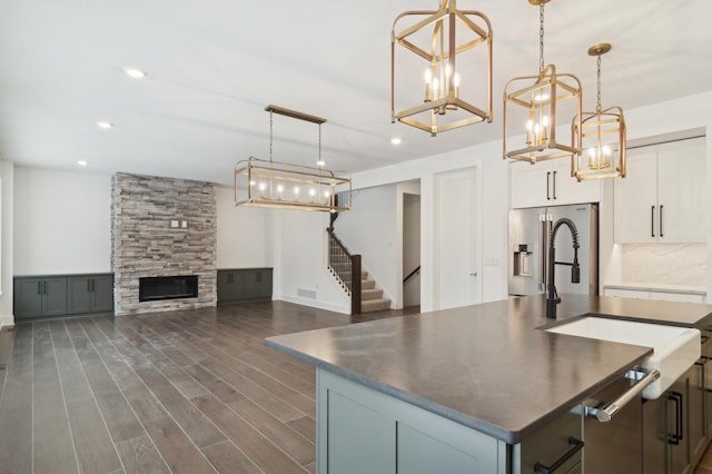 kitchen featuring a kitchen island with sink, a sink, dark countertops, dark wood-style floors, and high end refrigerator